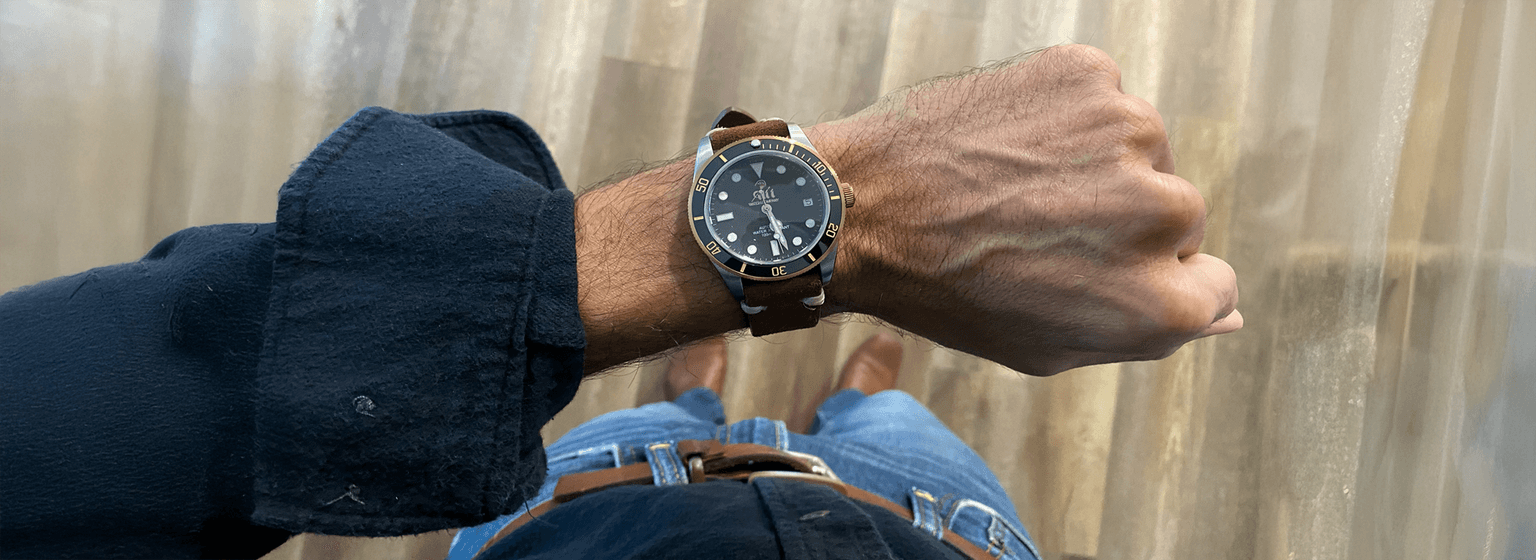 A black watch on a man's wrist with a wood floor background.