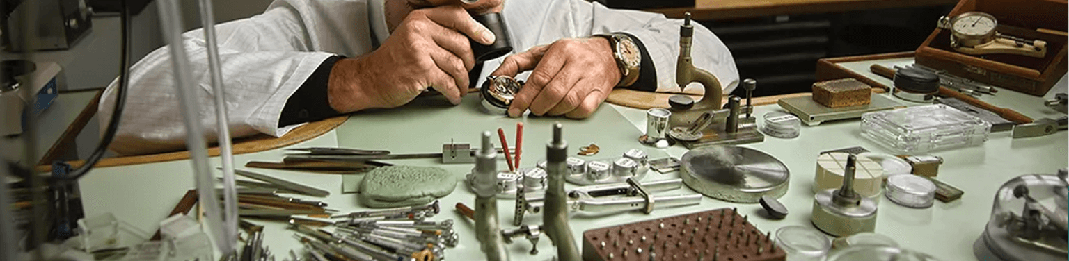 A watchmaker inspects a movement at his work bench.