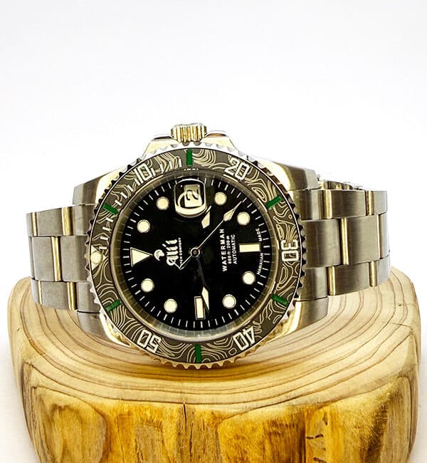 Ali'i Watch Company Waterman watch with a black bezel and carbon fiber bezel with green minute markers sits on a piece of wood.